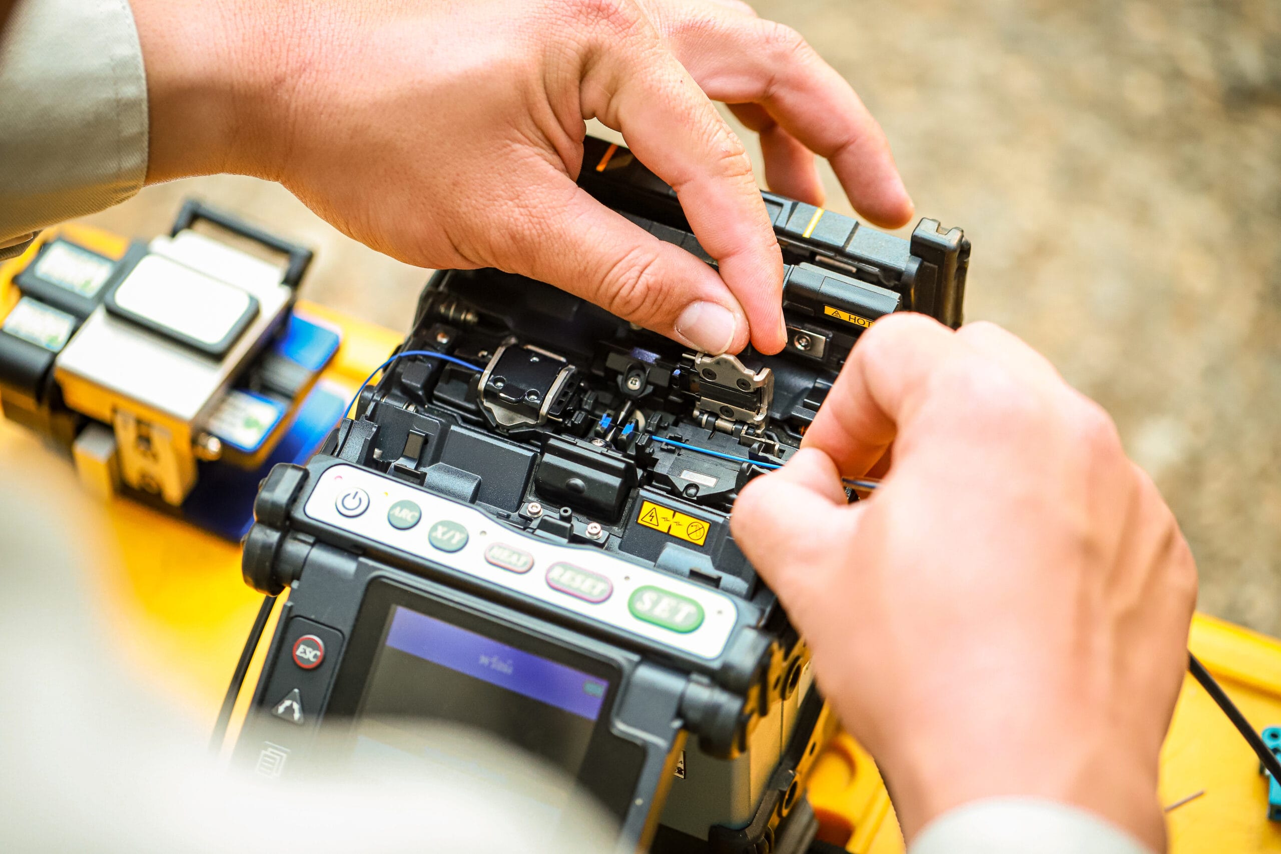 Close-up of hands operating a fiber fusion splicer on site