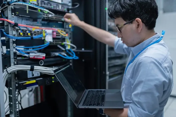 Engineer reaching into an open rack of cables while holding a laptop