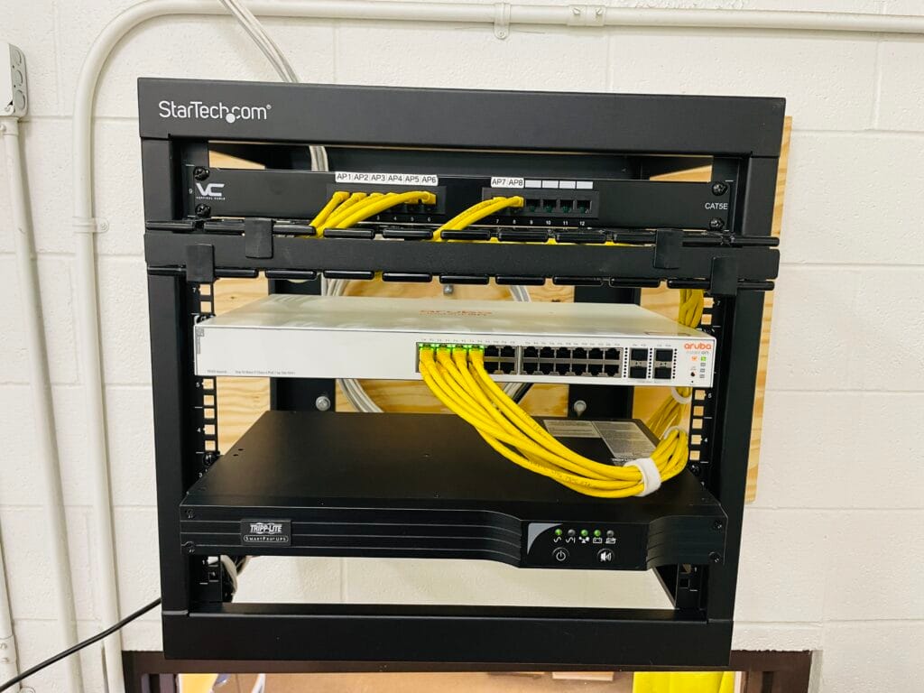 CAT5E patch panel and Aruba PoE switch patched with yellow cables above a Tripp-Lite UPS